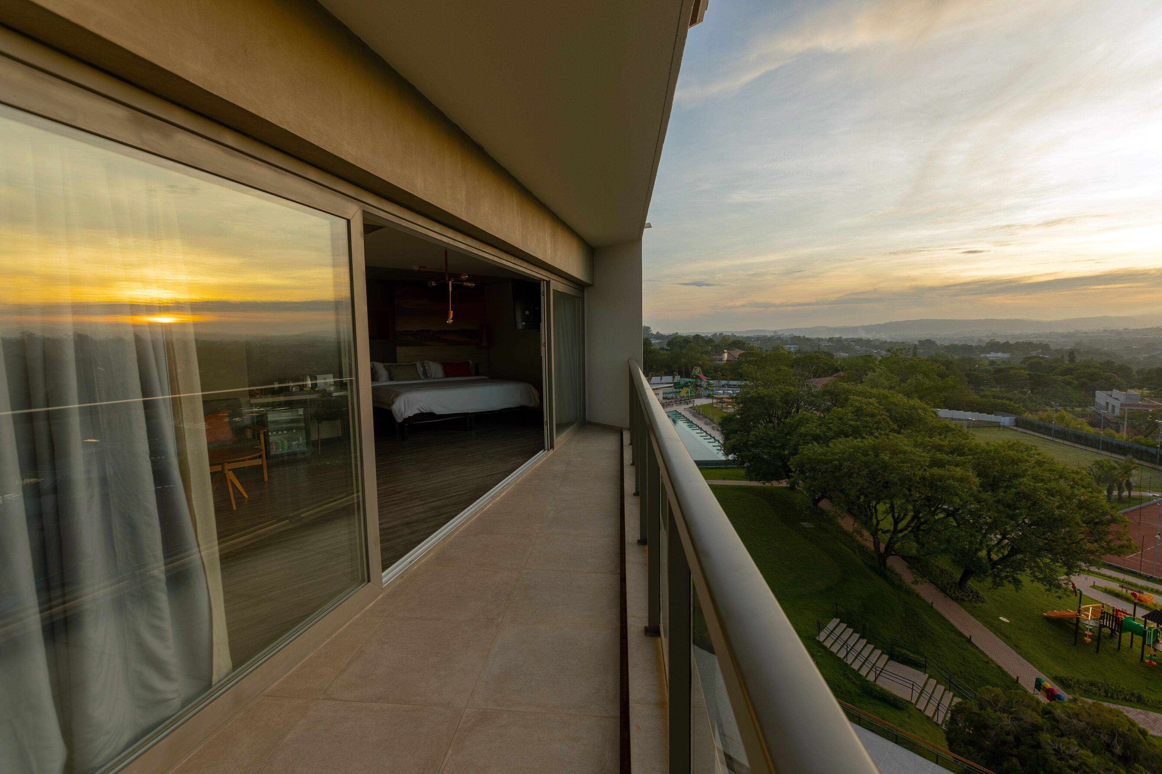 A balcony with a bed, a view of the city, and a grassy area with playground equipment.