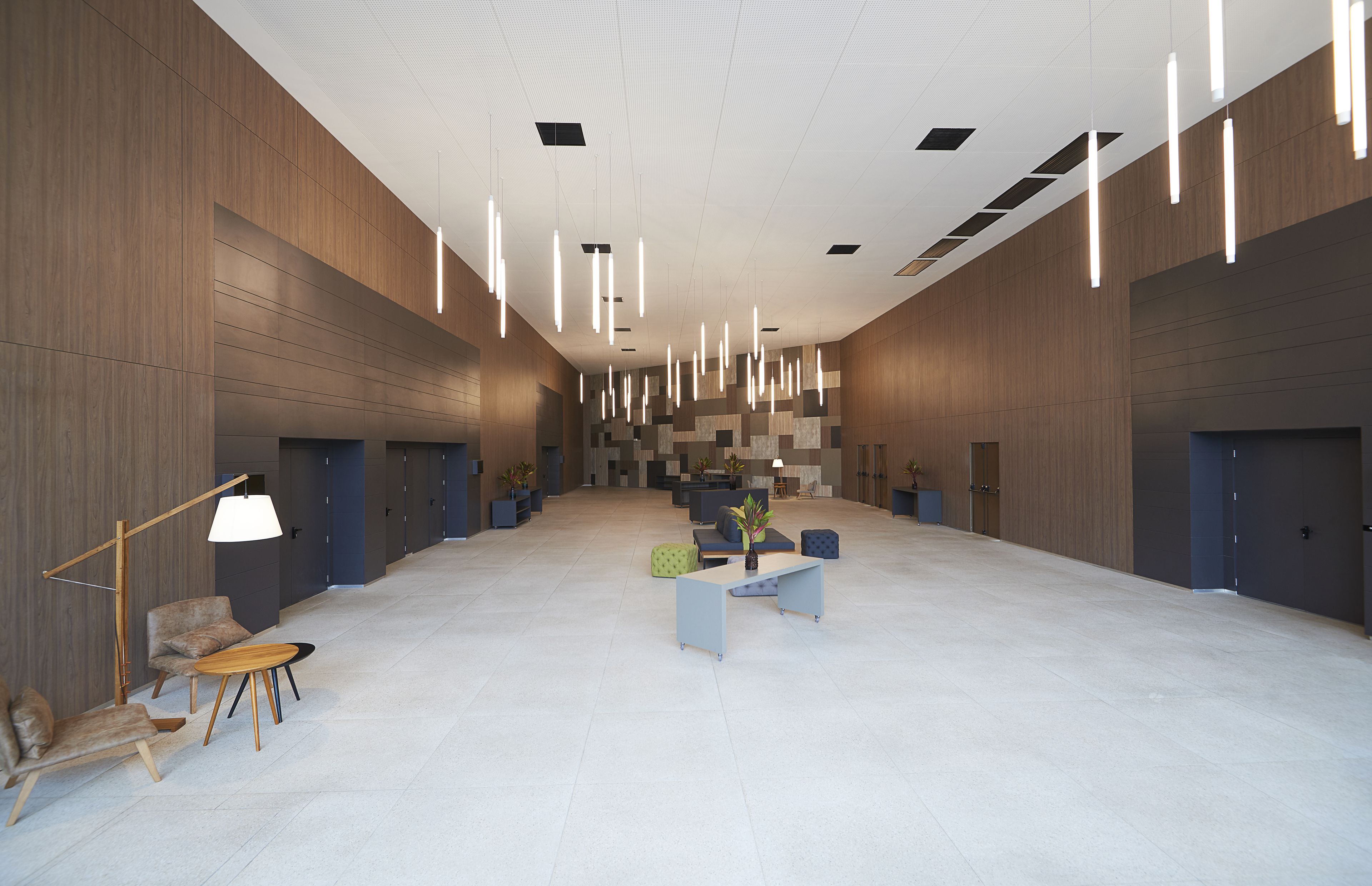 A spacious lobby with modern furniture, a central seating area, and a high ceiling with hanging lights.