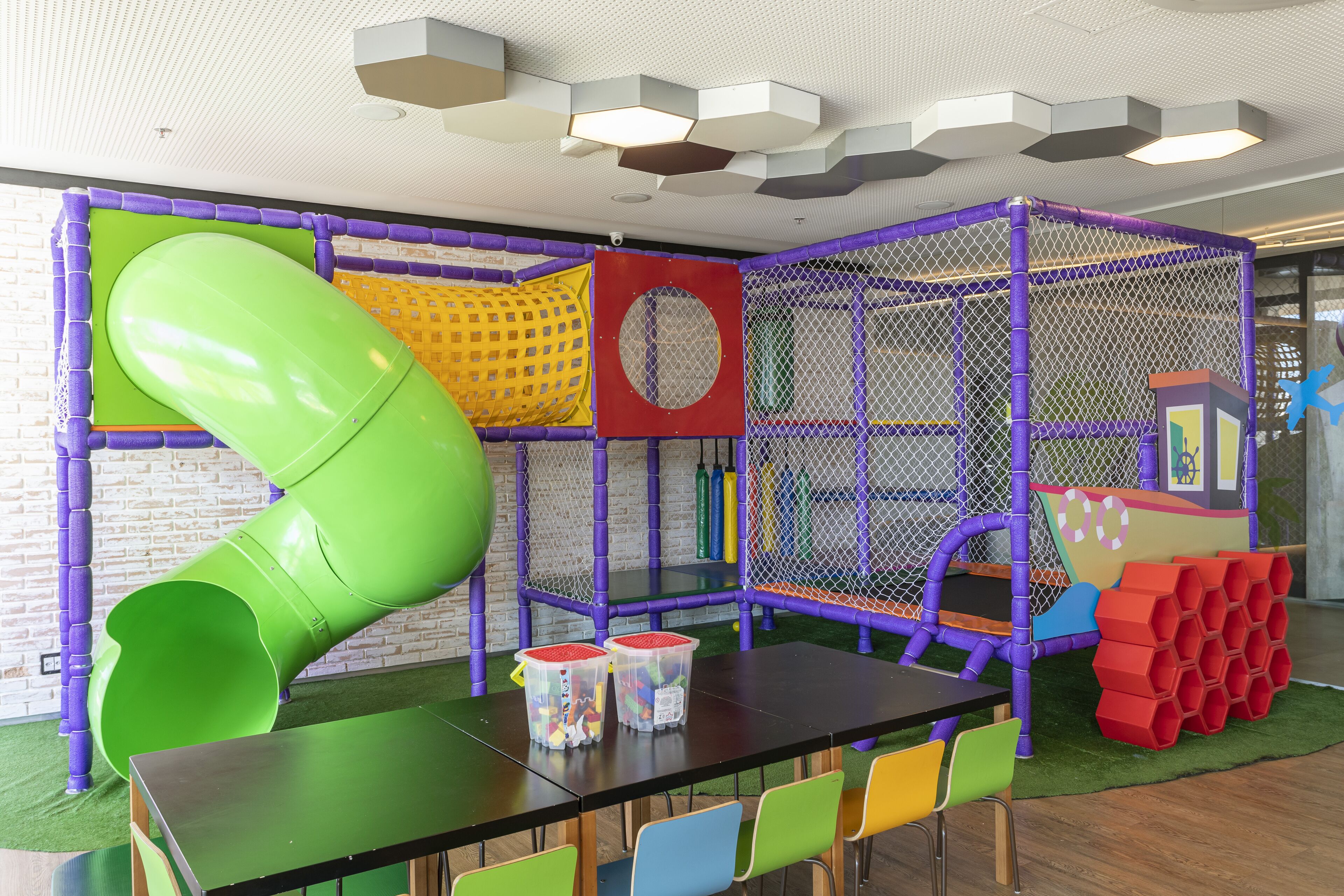 A play area with a green slide, netted play structures, and a table with chairs.