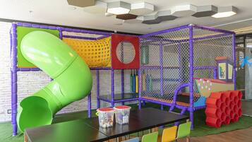 A play area with a green slide, netted play structures, and a table with chairs.