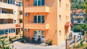 A multi-story hotel with balconies, a sign indicating a restaurant, and a mountainous backdrop. - Apartments Marinero (Kotor)