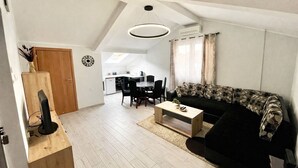 A modern living room with a black sofa, a wooden coffee table, and a dining area with a white table and chairs. - Apartments Marinero (Kotor)
