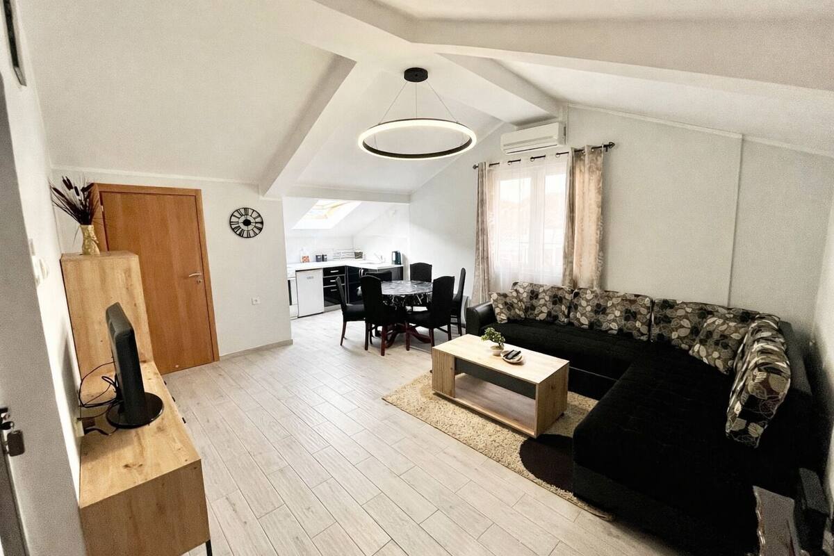 Una sala de estar moderna con un sofá negro, una mesa de centro de madera y un comedor con una mesa y sillas blancas.
