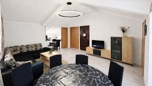 A modern living room with a sofa, a dining table, and a TV. There is a kitchen in the background. - Apartments Marinero (Kotor)