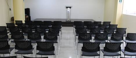 A conference room with rows of black chairs, a podium, and a projector screen.