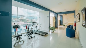 Une salle de sport moderne, dotée d’équipements d’exercice, de grandes fenêtres et offrant une vue sur la ville.