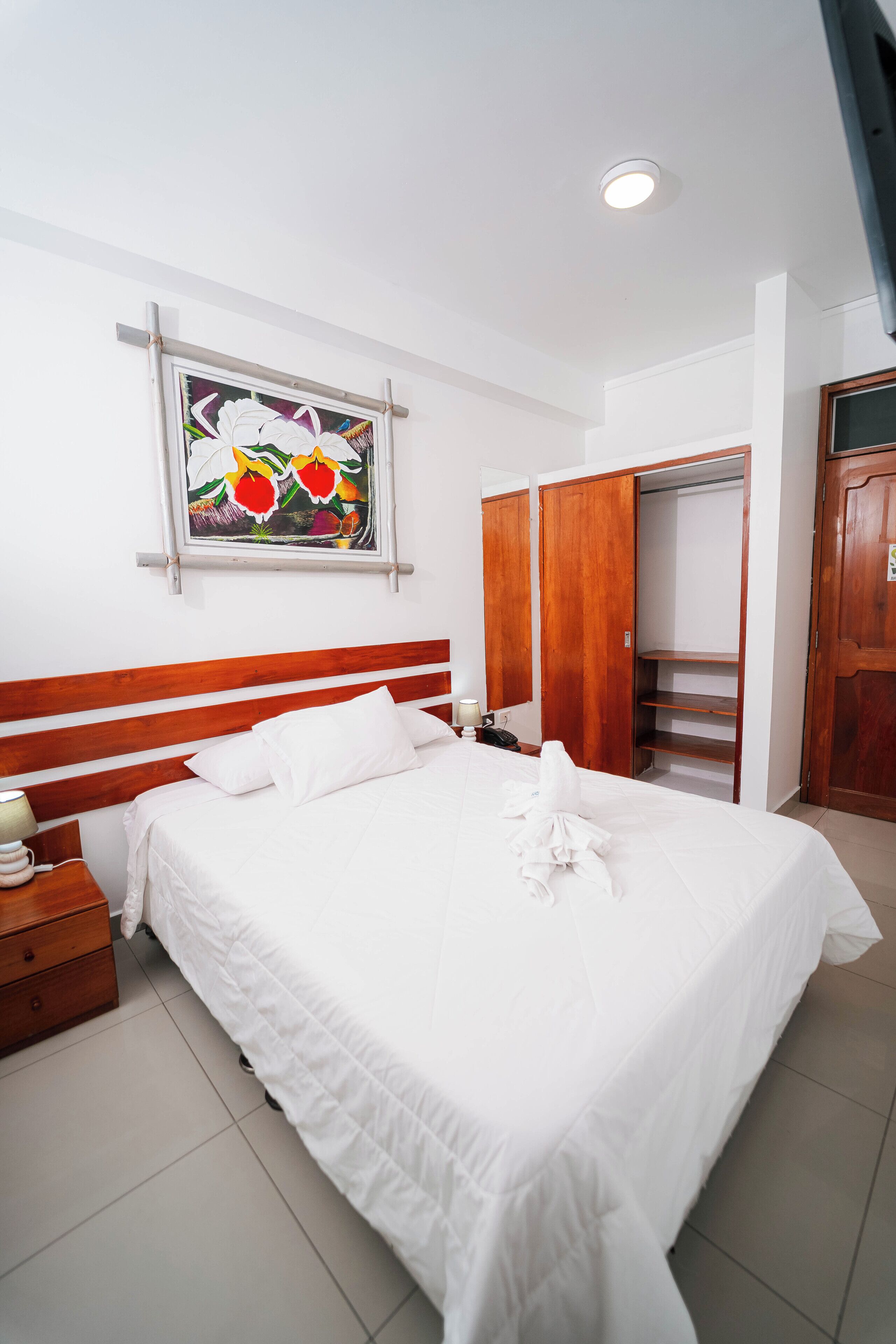 A neatly made bed with white linens, a wooden headboard, and a colorful painting above it.