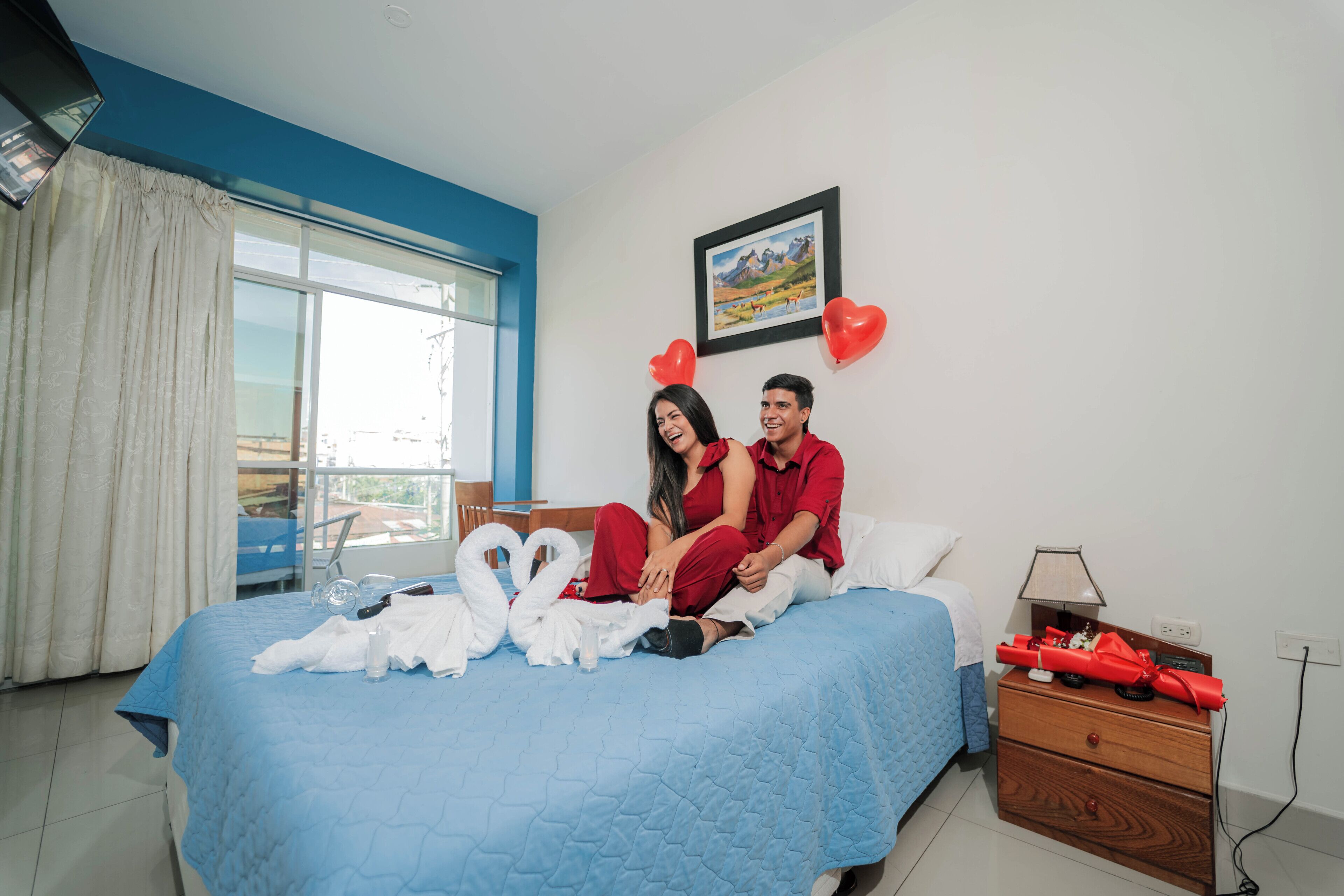 Un dormitorio con cama, mesita de noche, ventana con cortinas e imagen enmarcada en la pared.