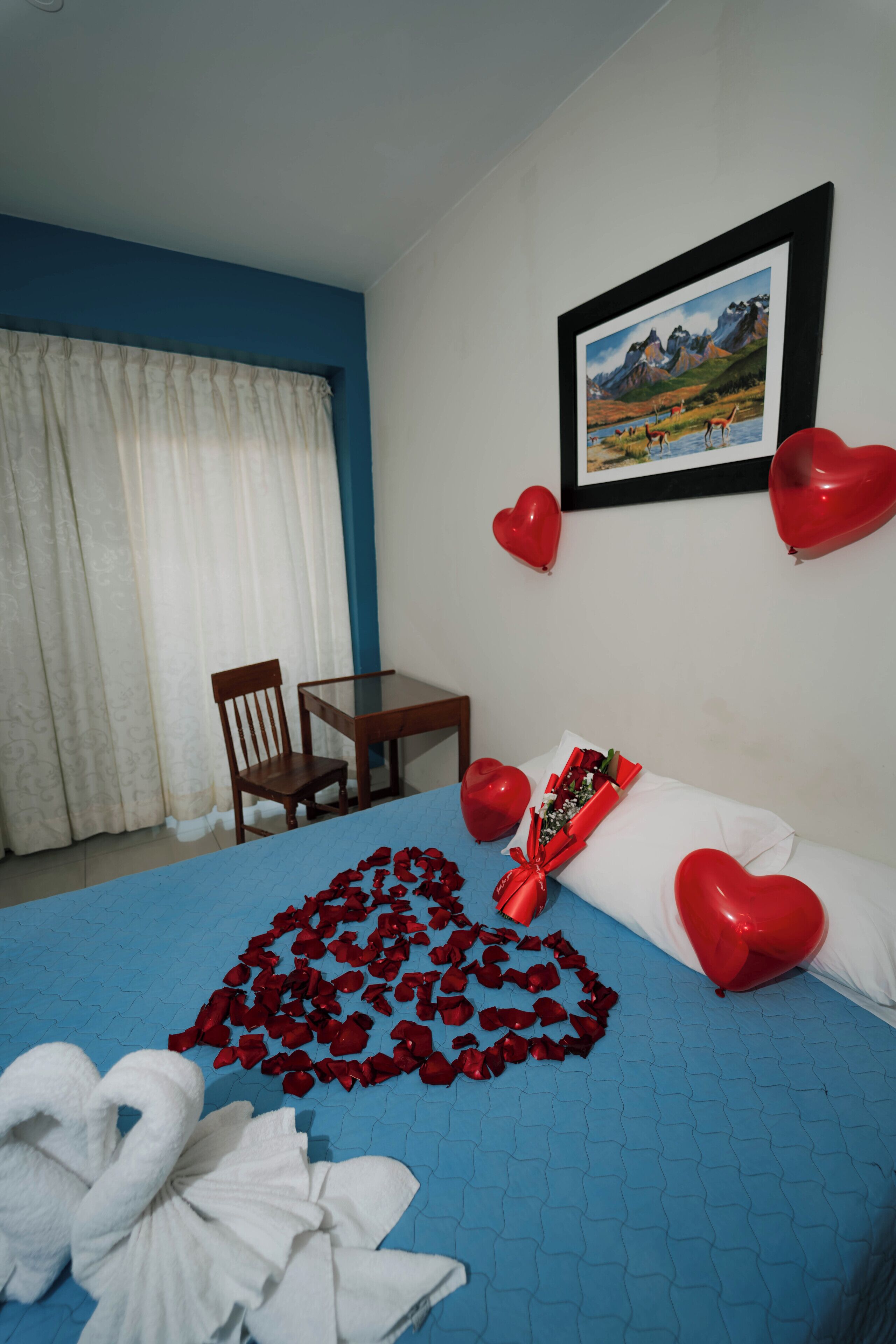 A hotel room with a bed, a framed picture on the wall, a table, and a chair.