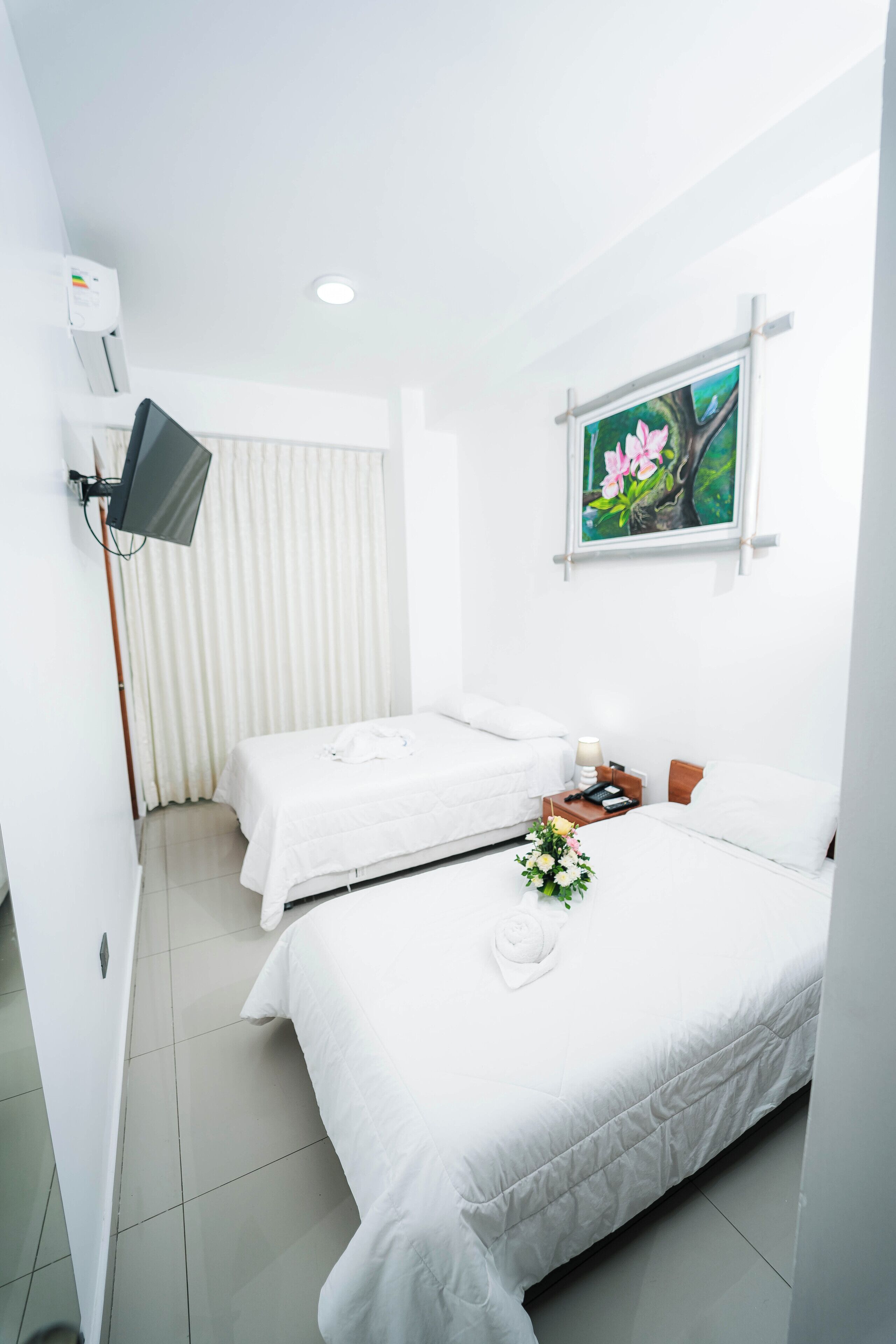 A hotel room with two beds, a TV, a painting, and a flower arrangement.