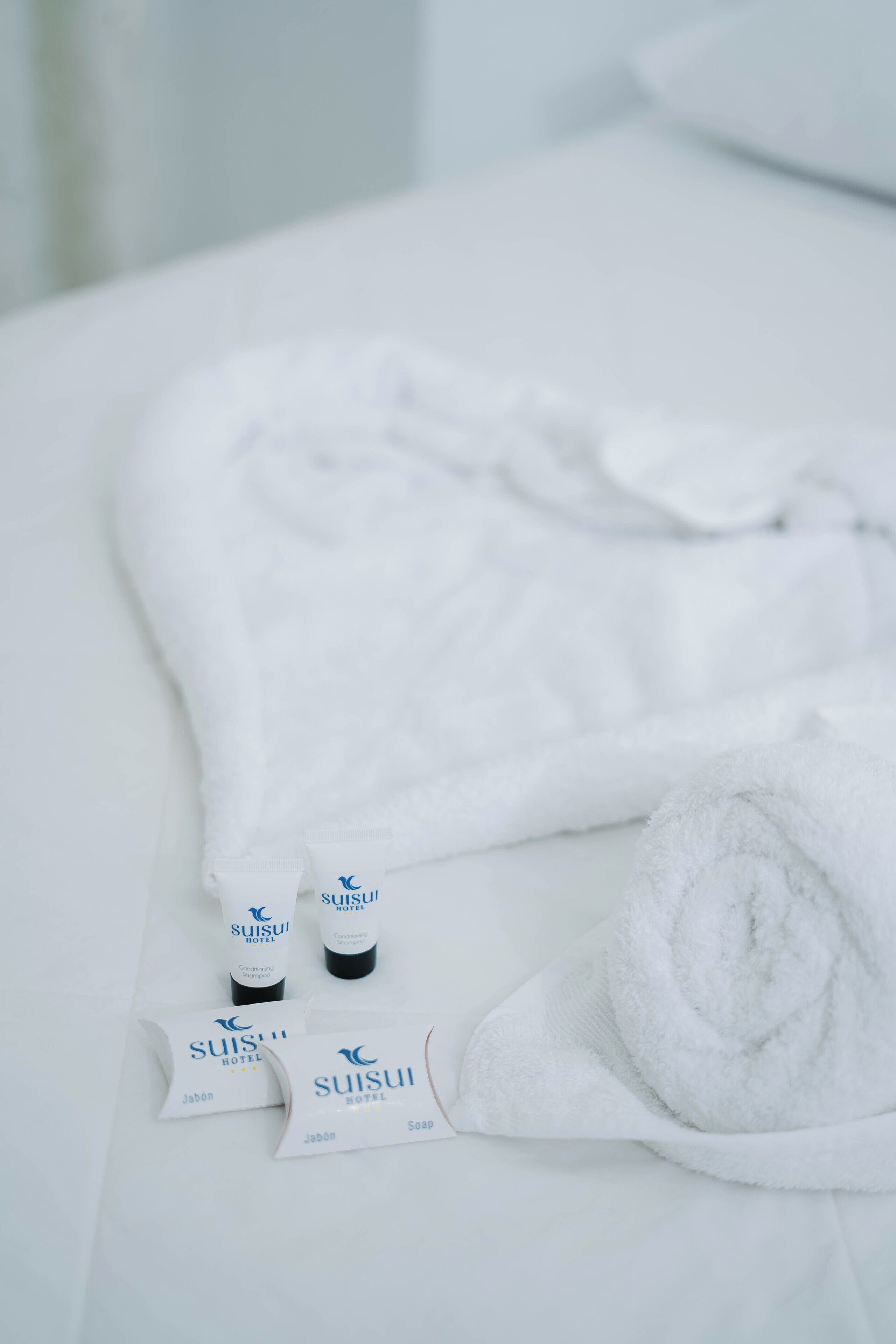 Un ensemble d’articles de toilette soigneusement disposés sur une surface blanche, comprenant une serviette blanche pliée, deux flacons de savon de l’hôtel Suisui et deux échantillons de savon de l’hôtel Suisui.