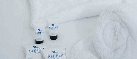 Un ensemble d’articles de toilette soigneusement disposés sur une surface blanche, comprenant une serviette blanche pliée, deux flacons de savon de l’hôtel Suisui et deux échantillons de savon de l’hôtel Suisui.