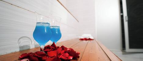 A wooden table with two glasses of blue liquid and scattered rose petals.