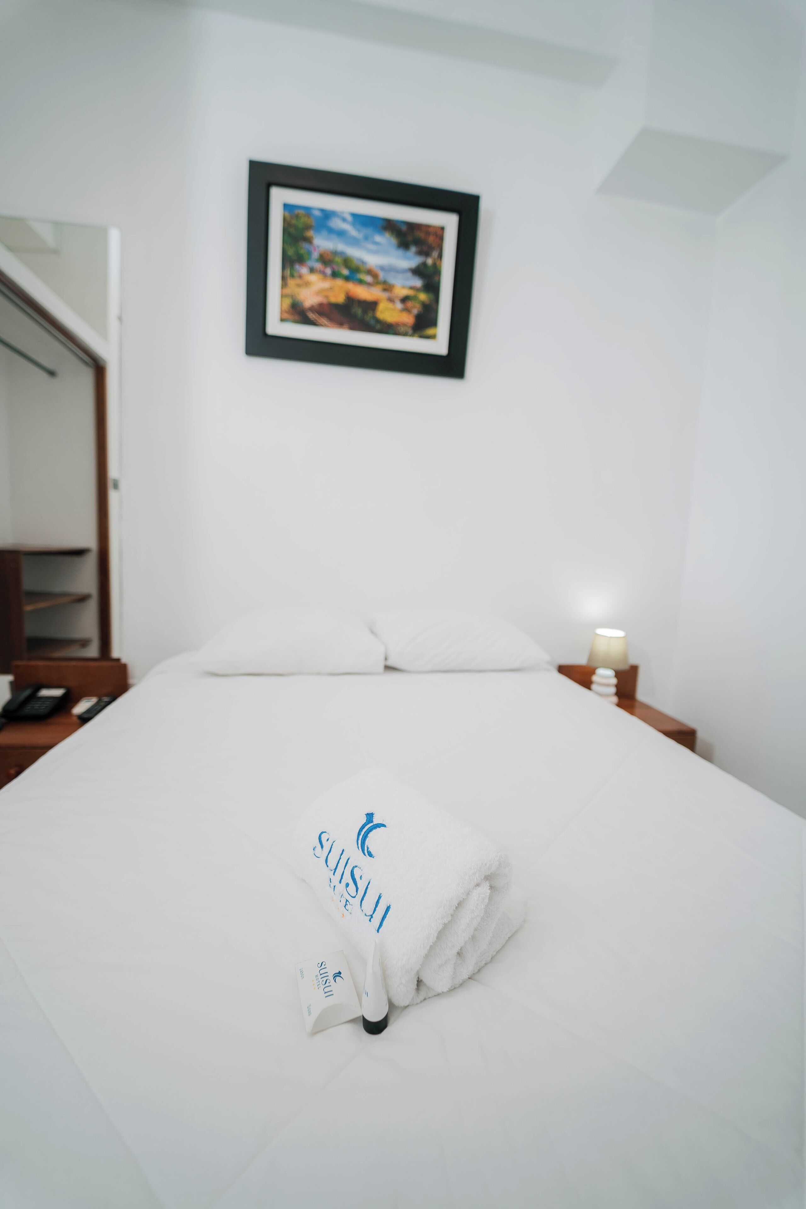 A neatly made bed with a folded towel and a framed picture above it.