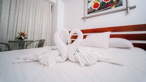Une chambre d’hôtel avec un lit, un tableau, une fenêtre avec des rideaux et une petite table agrémentée de fleurs.