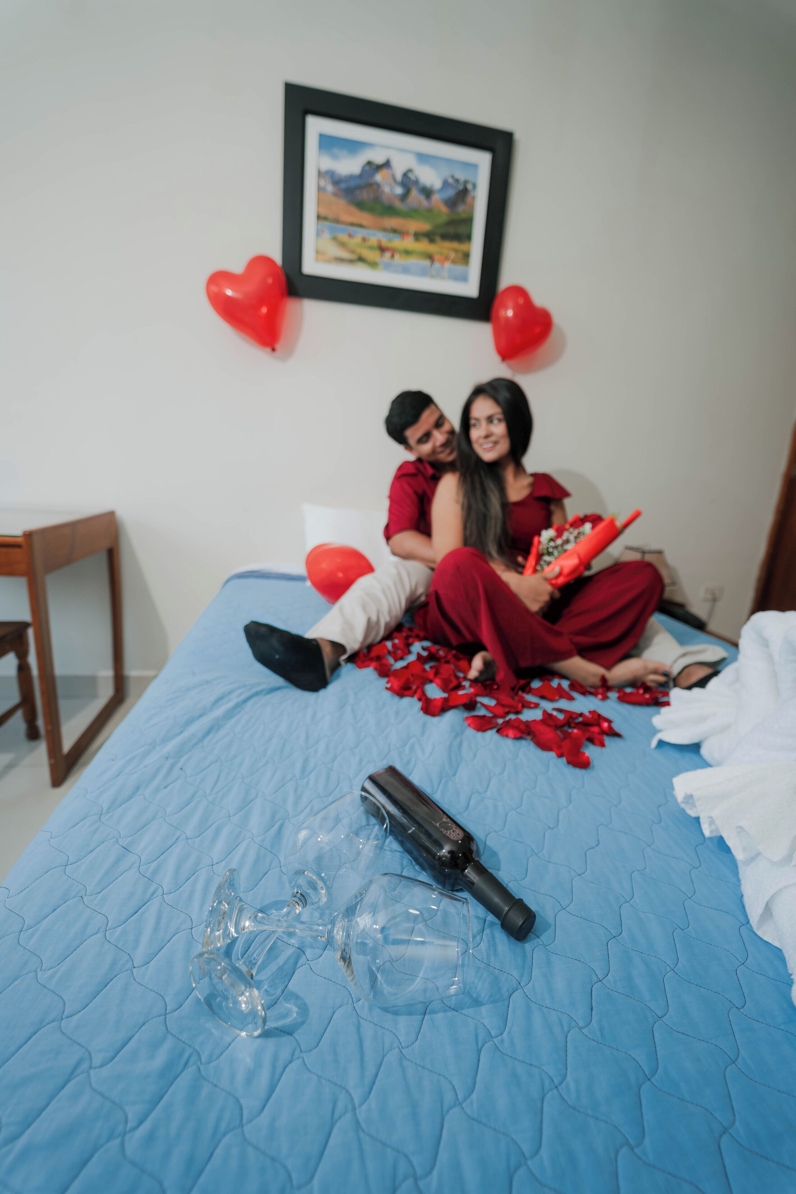 Un letto con una coperta blu, un quadro appeso al muro e due palloncini a forma di cuore rossi.