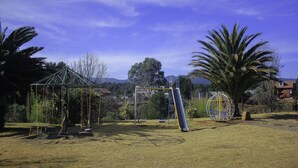A playground with swings, a slide, and a climbing structure in a grassy area with trees and houses in the background. - Hotel Kuautli (Huasca de Ocampo)