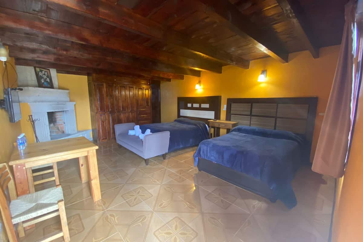 A room with two beds, a wooden desk, a chair, a fireplace, and a tiled floor.