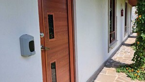A wooden door with a keypad lock, a stone-paved walkway, and a covered corridor with windows. - Hotel Kuautli (Huasca de Ocampo)