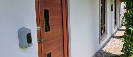 Una puerta de madera con cerradura electrónica, un camino empedrado de piedra y un corredor cubierto con ventanas.