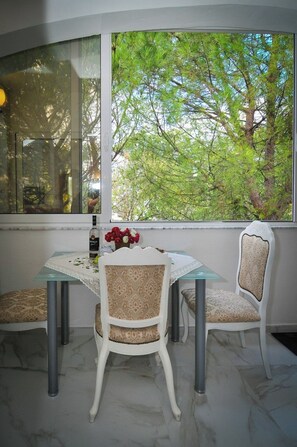 Uma área de refeições com mesa e cadeiras, uma garrafa de licor e um vaso com flores.