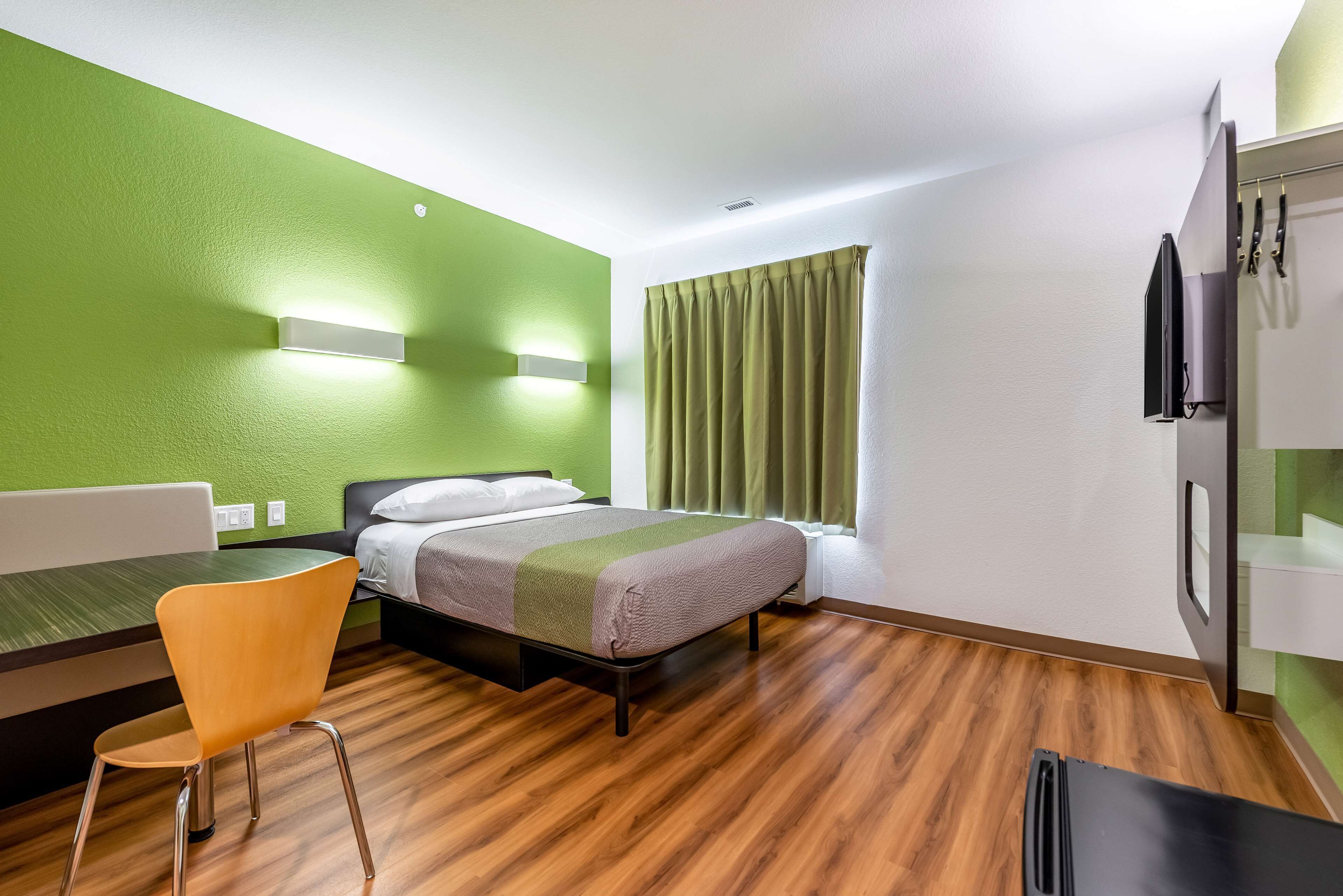 Una habitación de hotel con cama, una silla, un escritorio y ventana con cortinas.