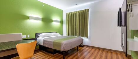Una habitación de hotel con cama, una silla, un escritorio y ventana con cortinas.