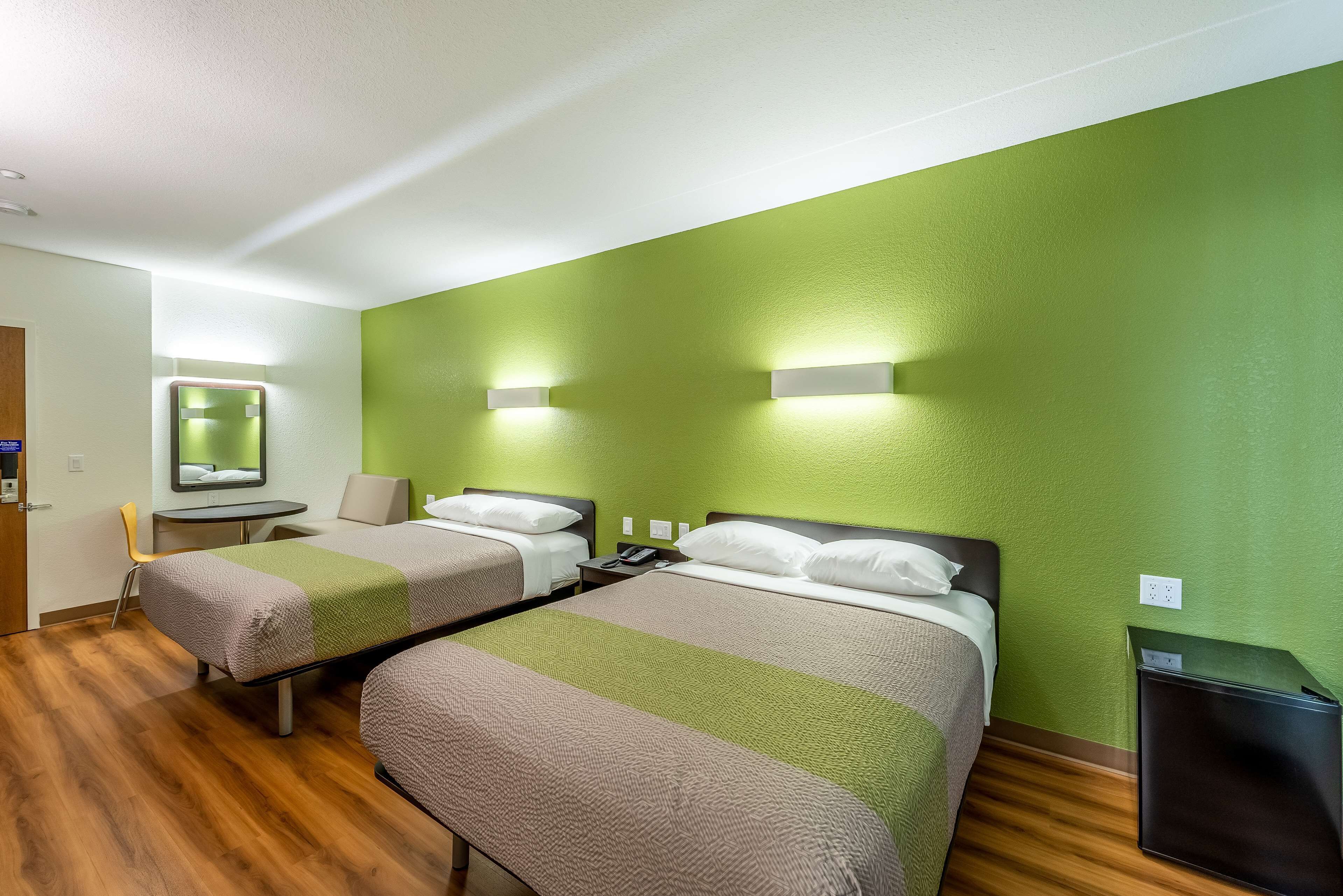 Habitación de hotel con dos camas, una mesita pequeña, una silla, un espejo y un cubo de basura.