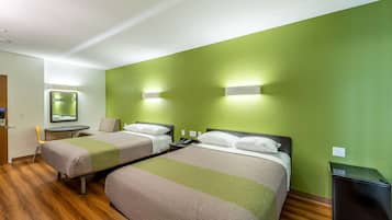 Een hotelkamer met twee bedden, een tafeltje, een stoel, een spiegel en een prullenbak.