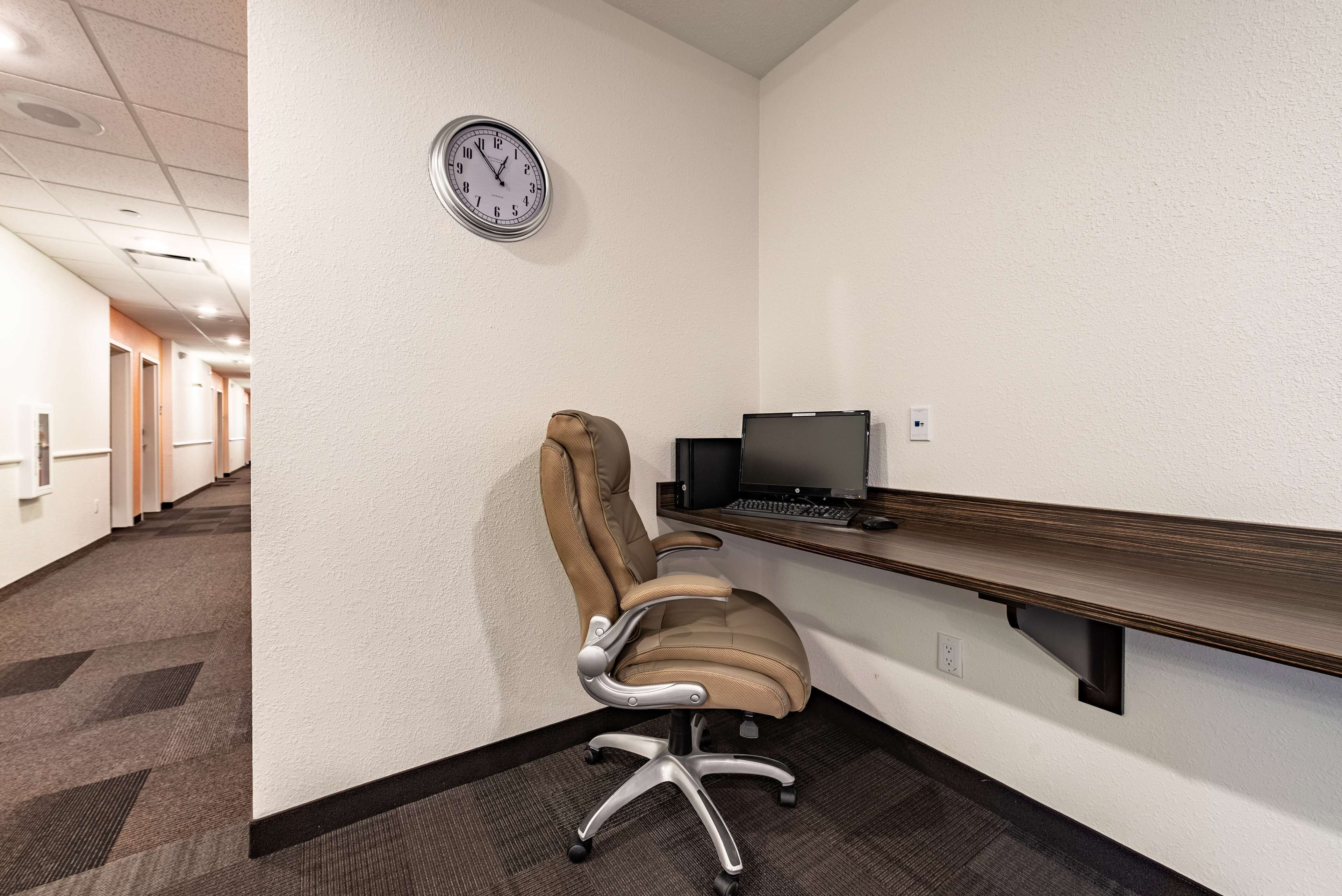 A conference room with a high-backed chair, a desk with a computer, and a clock on the wall.
