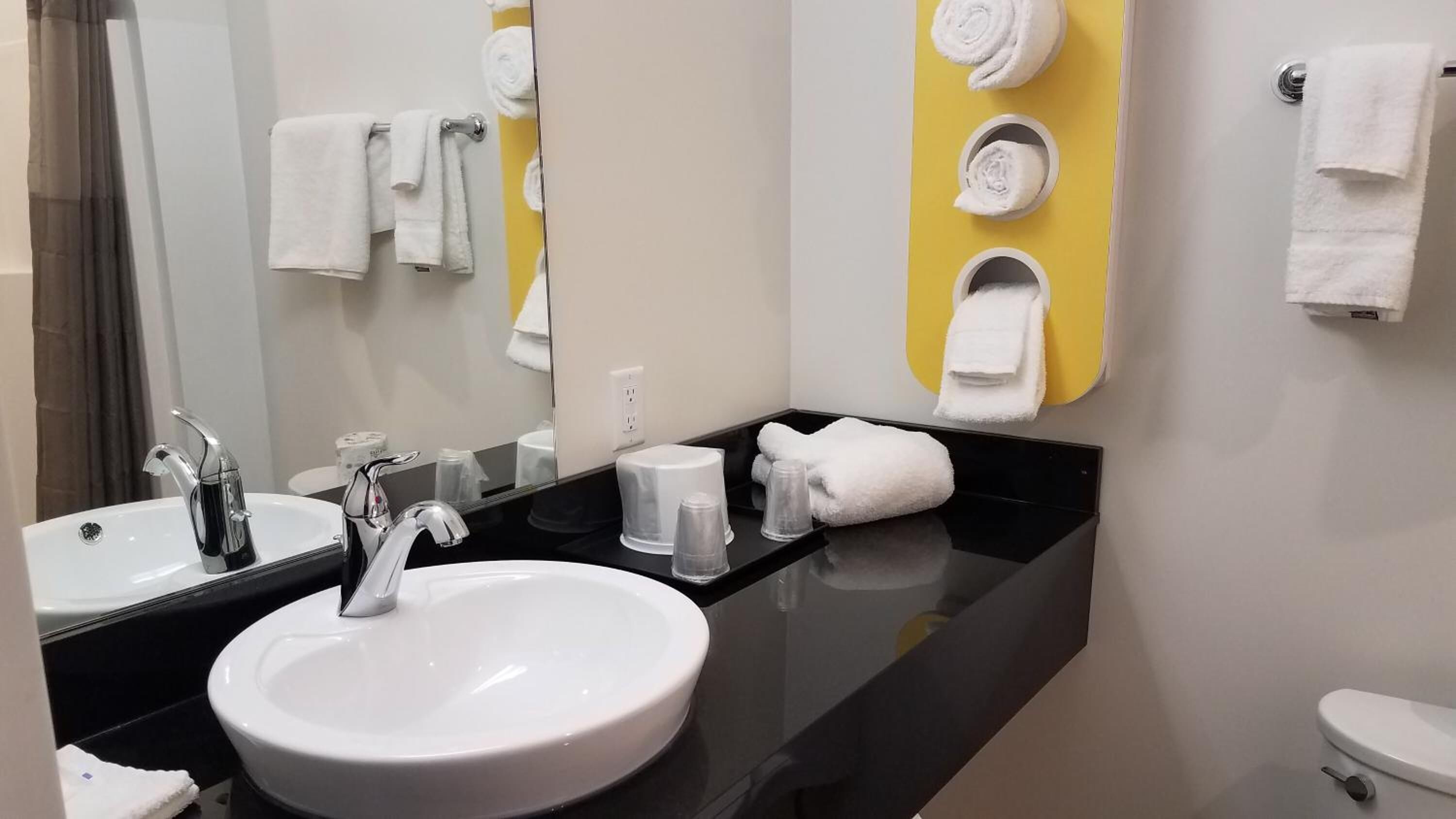 Een moderne badkamer met een zwart aanrecht, twee wastafels, een toilet en een spiegel.