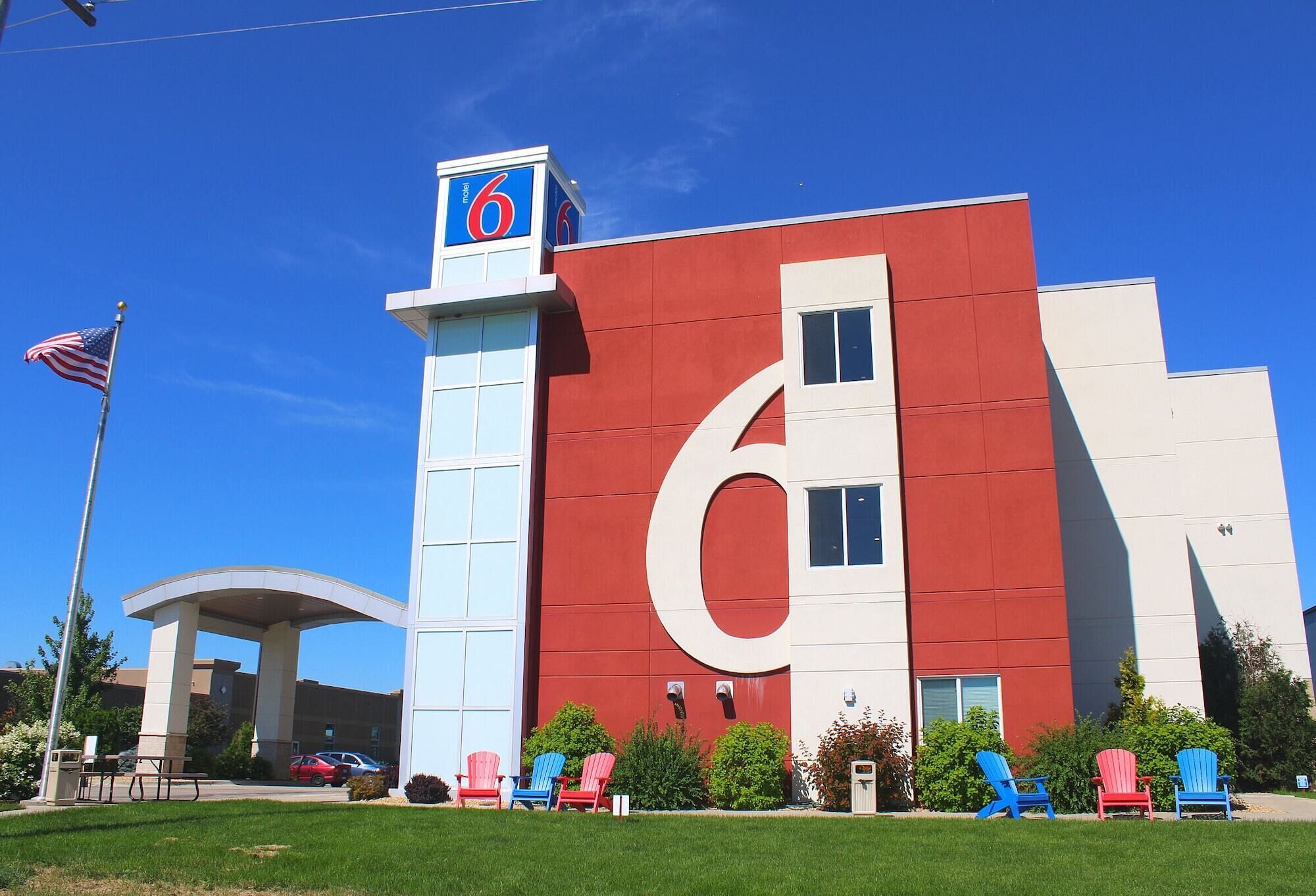 A modern building with a large '6' sign, outdoor seating with colorful Adirondack chairs, and an American flag.