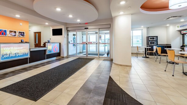 A hotel lobby with a reception desk, a waiting area with chairs, a play area, and a view of the outside through the glass doors.