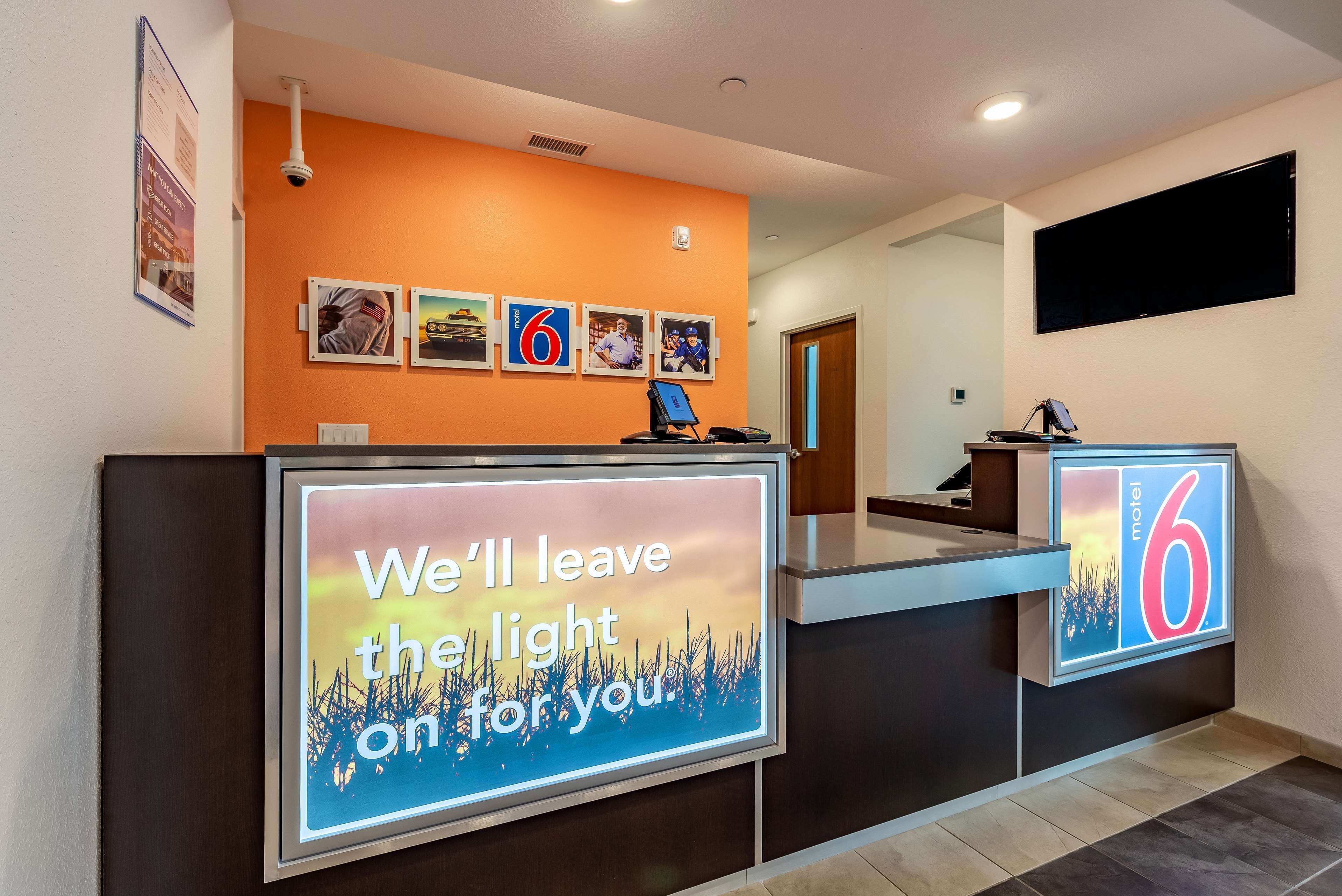 A hotel reception area with a large digital sign displaying a welcoming message, a number '6' sign, and a series of framed pictures on the wall.