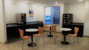 A modern kitchen with a coffee machine, microwave, and a large window with a view. There are four chairs and a small table in the center.