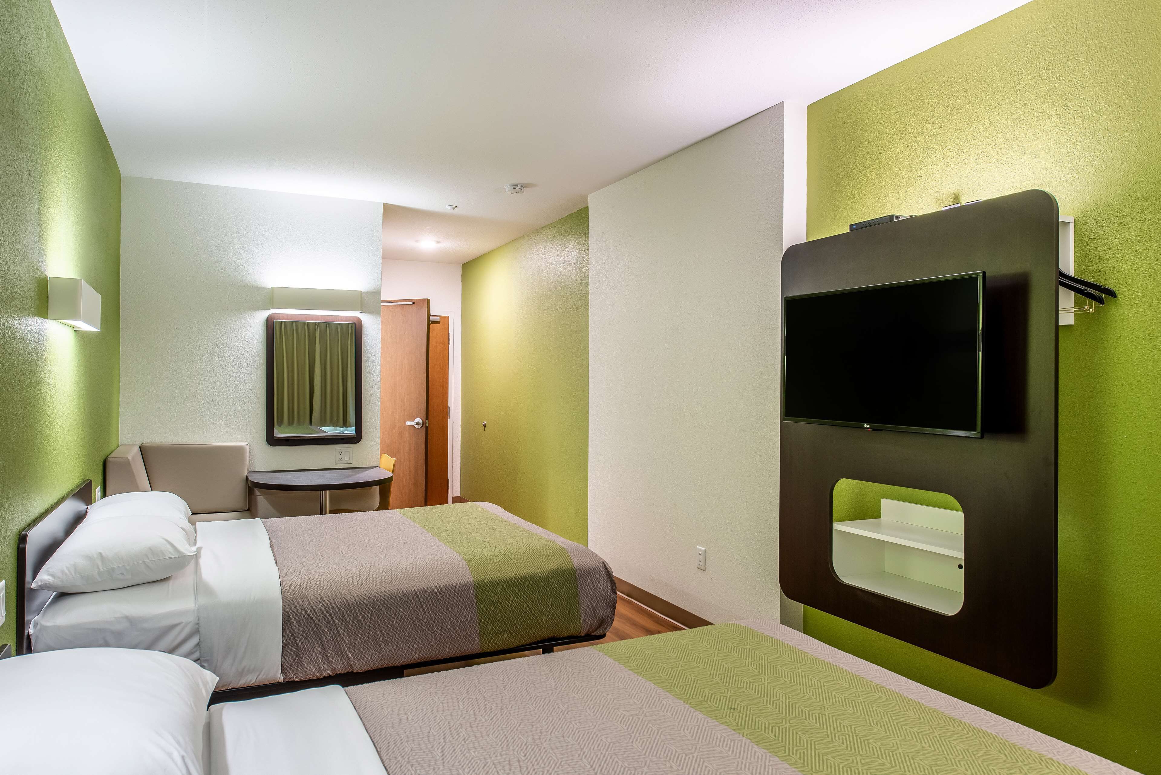 Ein Hotelzimmer mit zwei Betten, einem an der Wand befestigten Fernseher und einem kleinen Tisch mit Stuhl.