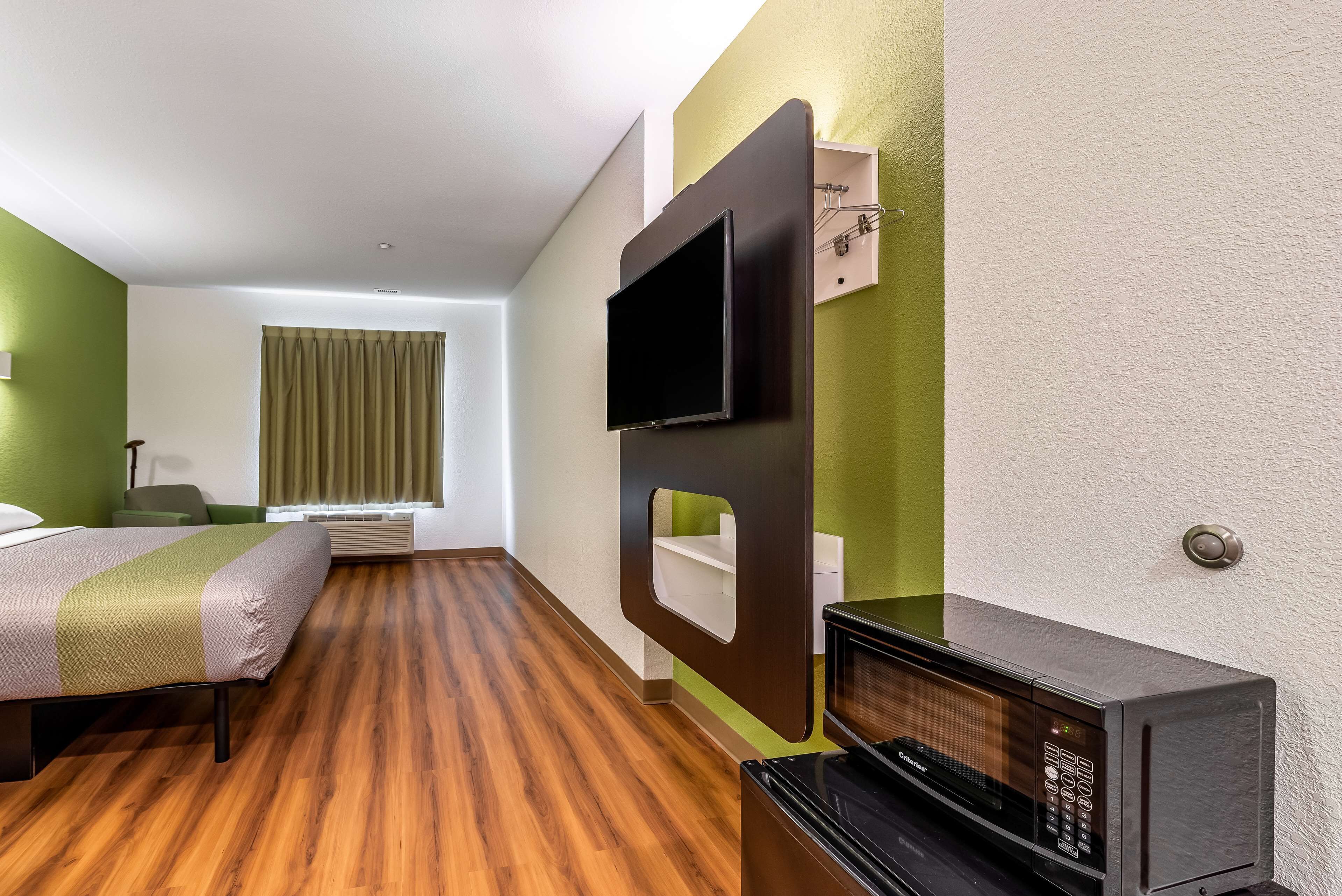 A hotel room with a bed, a flat-screen TV mounted on the wall, a microwave, and a window with curtains.