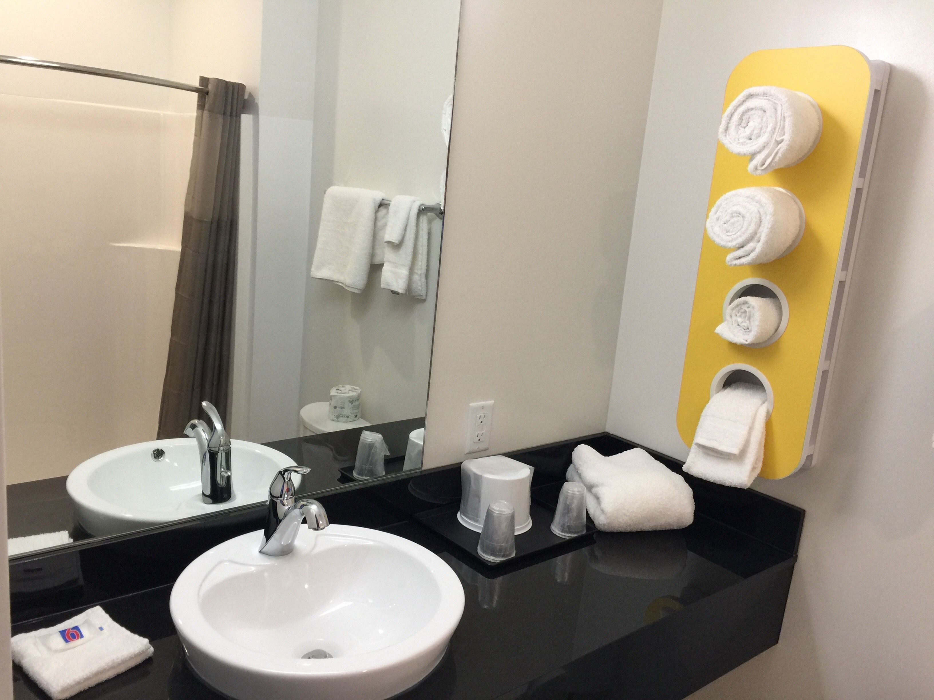 A bathroom with two sinks, a mirror, a shower, and a towel rack with towels.