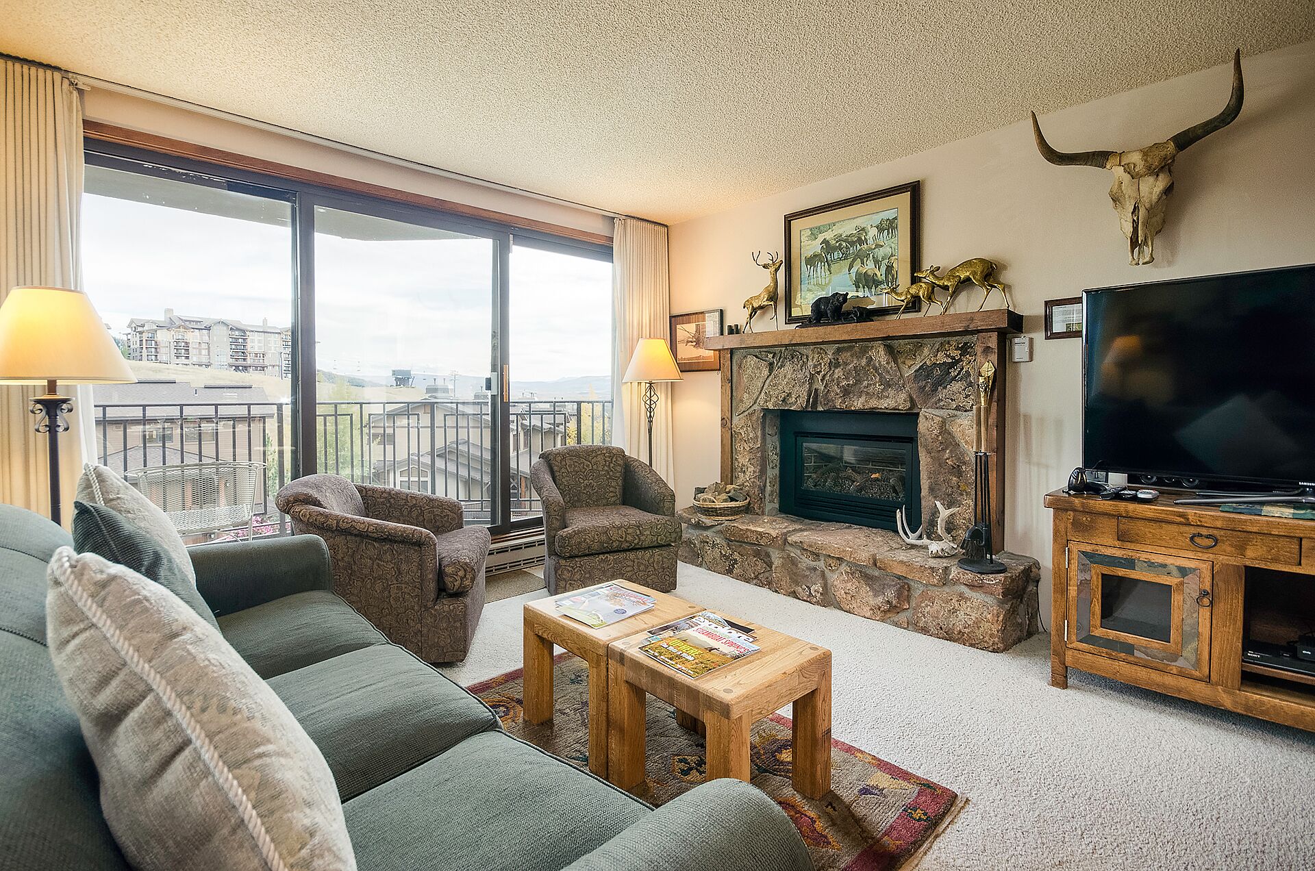 A living room with a fireplace, a television, and a balcony with a view.