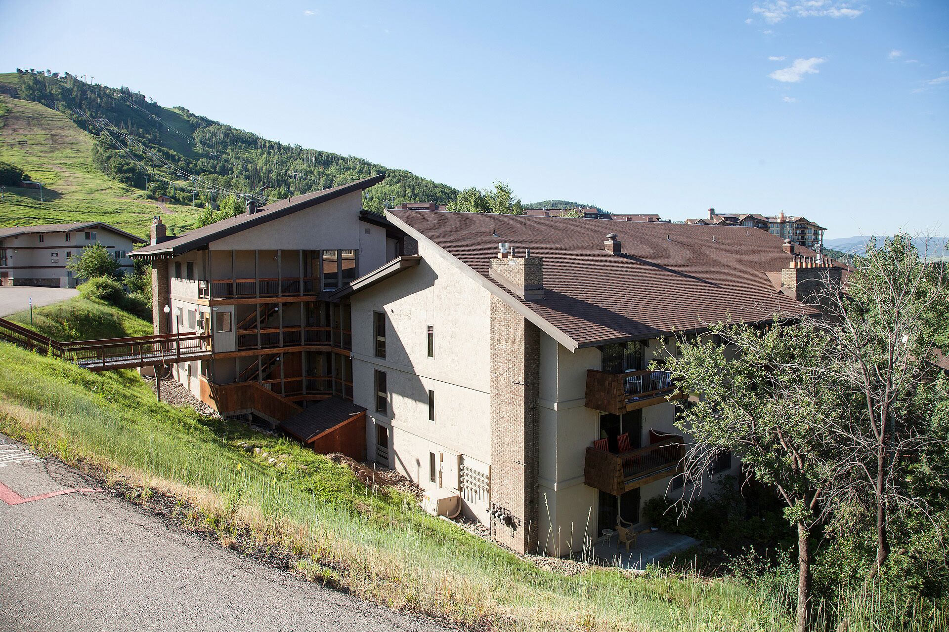 A multi-story building with a sloped roof, a staircase leading to the upper floor, and a view of a hillside.