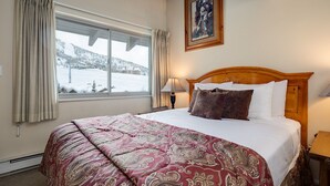 Een hotelkamer met een groot bed, een houten hoofdbord, een nachtkastje met een lamp, een raam met gordijnen en een ingelijst beeld aan de muur.