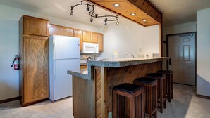 Una cocina con armarios de madera, un refrigerador blanco, un microondas, una encimera de granito y taburetes de bar.