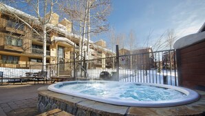 Un jacuzzi rodeado de muros de piedra, con una valla metálica y un edificio al fondo.