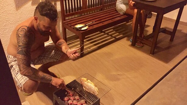 Un homme fait griller des saucisses sur un barbecue portable, à l’extérieur.
