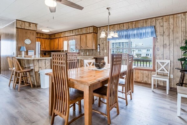 A modern kitchen with wooden cabinets, a central island, and a dining area with wooden chairs. - Beach Front House | Dog-Friendly | Stunning Sunrise & Sunset Views | Sleeps 10 (Gulf Shores)