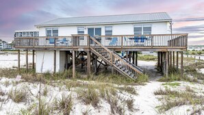 A beachfront house with a wooden deck and stairs leading to a balcony.