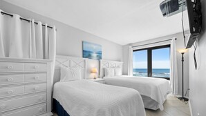 A hotel room with two beds, a dresser, a painting, a lamp, and a view of the ocean. - Island Sunrise 362-The Beach is Where You Need to Be! (Gulf Shores)