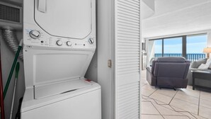 A laundry room with a washing machine and dryer, a window, and a balcony with a sofa and a lamp. - Island Sunrise 362-The Beach is Where You Need to Be! (Gulf Shores)