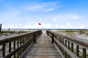 A wooden boardwalk leading to a beach with a red flag on a pole.