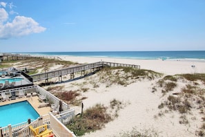 A beach with a wooden boardwalk, a swimming pool, and beach chairs.